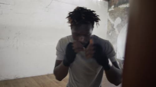 Selbstbewusster Boxer, der im Fitnessstudio aktiv aus nächster Nähe auf die schwere Tasche schlägt