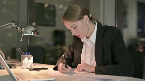 Woman Writing at Desk in Modern Office at Night