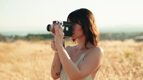 Woman Filming with Vintage Camera in Grassy Field