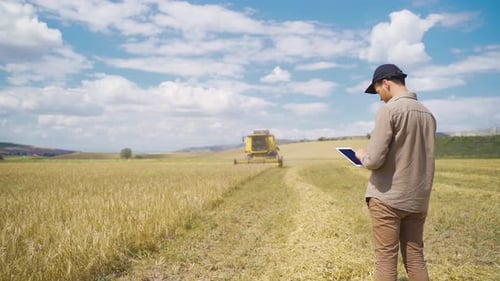 Man Using Tablet on Farm with Harvester