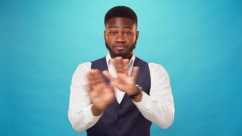 Un jeune afro-américain rejette quelque chose avec les mains croisées et dit « non » sur fond bleu