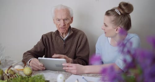 Senior Man and Young Woman Using Tablet at Table