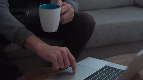 Man works on computer while holding a mug at home