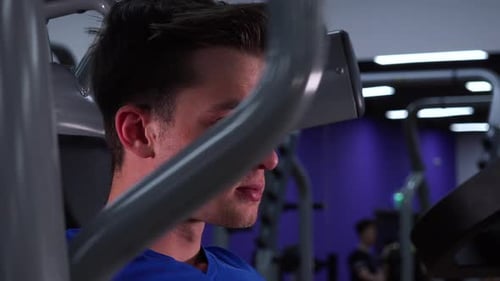 A Young Fit Man Trains on a Machine in a Gym - Face Closeup From the Side