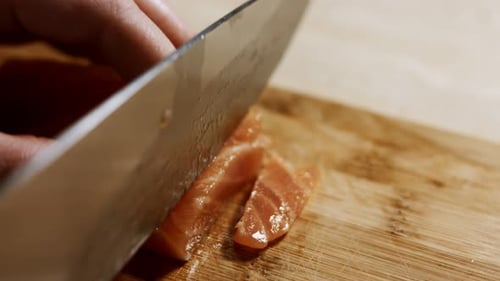 Closeup of Female Hand Slicing Fresh Salmon Fillet on a Wooden Board