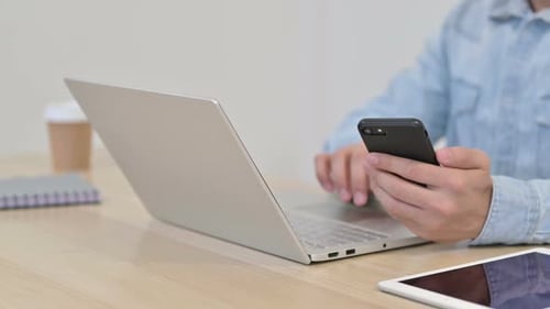 Mann benutzt Laptop mit Smartphone Nahaufnahme