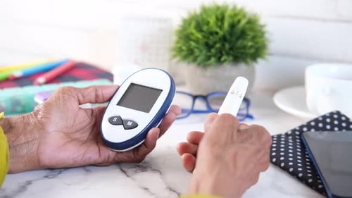 Adult Using Blood Glucose Meter on Table