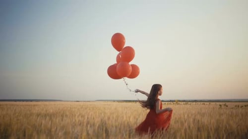 Happy Young Girl with Balloons Running in the Wheat Field at Sunset. Video.