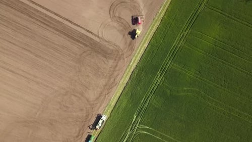 Top down aerial view of green tractor cultivating ground and seeding a dry field. Farmer preparing