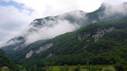 Green and cloudy alpine mountains over a lake at misty morning, panning shot
