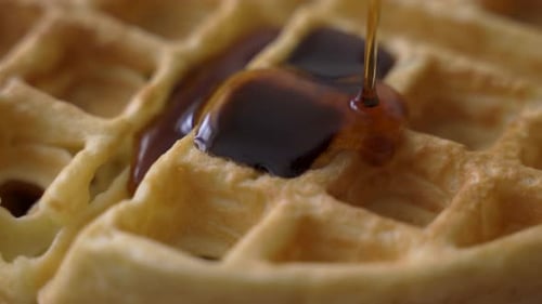 Vue macro en rotation rapprochée de gaufres dorées croustillantes arrosées de sirop d'érable sucré pour le matin