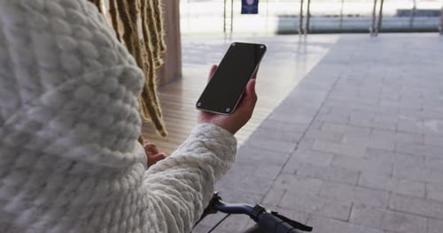 Mixed race man with dreadlocks wheeling bicycle in the street using smartphone