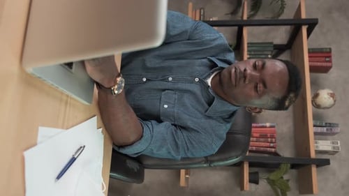 Vertical. African Man Employee Works in the Office at the Computer. Black Businessman Looking at