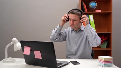 Man Working at Desk Puts on Headphones