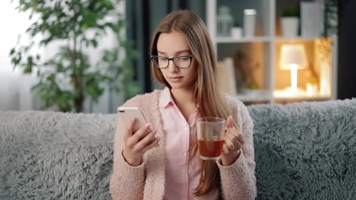 Woman Relaxes on Couch with Phone and Tea