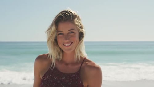 Mujer caucásica sonriendo en la playa y mirando a la cámara