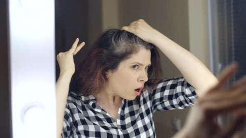 Worried Woman Examining Gray Hair Roots in Mirror