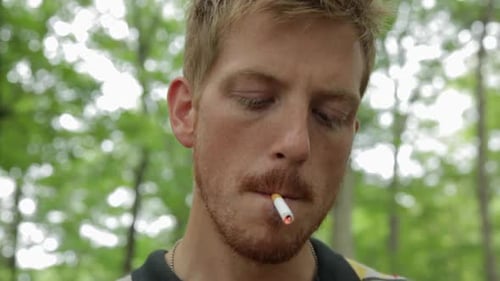 Homme adulte moyen fumant une cigarette dans la forêt
