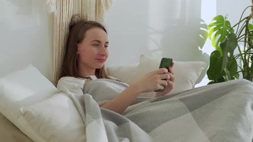 Relaxed Woman Using Smartphone in Bed at Home