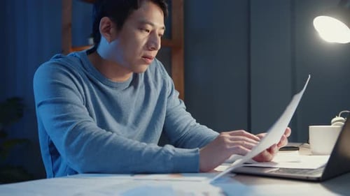 Man Works With Laptop and Documents at Night