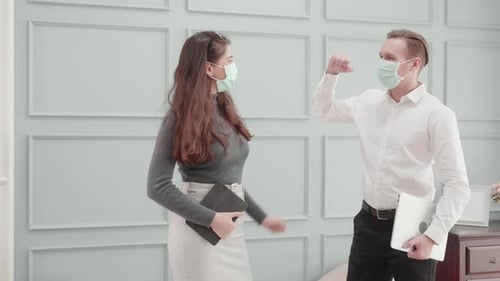 Young american business man and woman in face mask greeting with elbow bump at office.