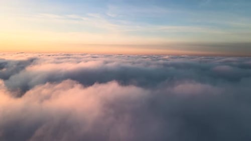 Aerial view of vibrant yellow sunrise over white dense clouds with blue sky overhead.