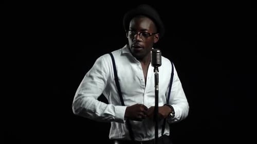 Cantante afroamericano masculino canta en un micrófono y baila. Fondo negro. Cámara lenta