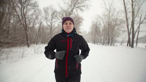 Sporty Woman Runs Through Forest in Winter and Checks the Indicators on a Fitness Bracelet Front