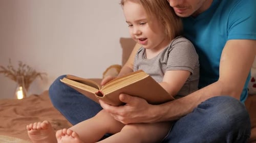 Father Reading Book with Little Girl on Bed