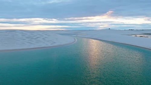 Un Drone passe au-dessus d'un magnifique lagon bleu avec des dunes de sable blanc à la fin de la journée colorée