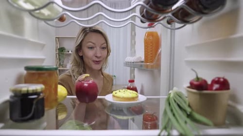 Woman Looks in Refrigerator and Eats Apple