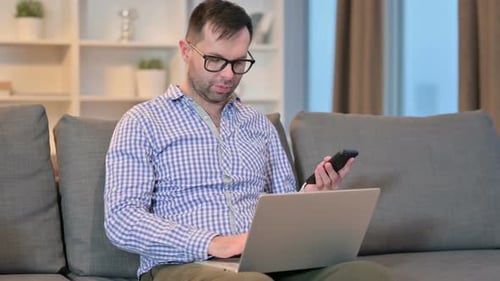 Man Using Laptop and Smartphone on Sofa