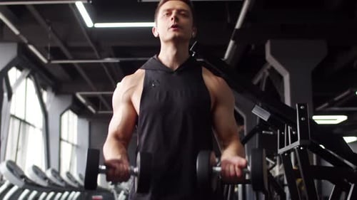 Joven musculoso entrena en el gimnasio levantando pesas con las dos manos, vista frontal. Hombre de complexión atlética