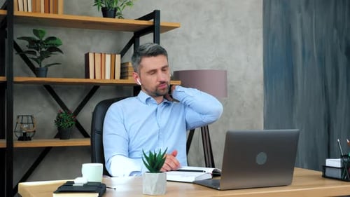 Tired businessman in home office massages neck rubs tense muscles after long time using laptop