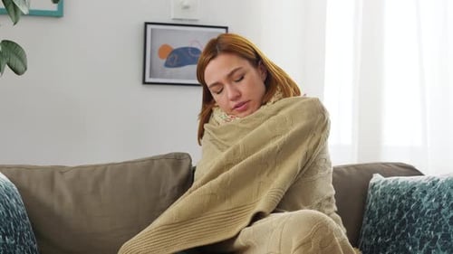 Femme malade triste dans une couverture et une écharpe à la maison