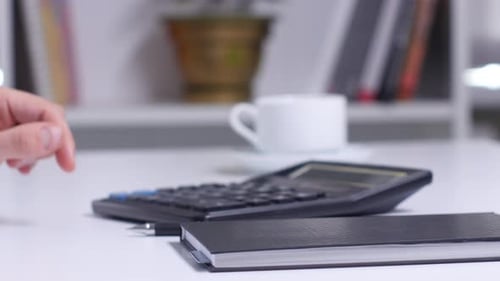 Man with Blueprint Counting on Calculator and Writing To Notebook. Close Up