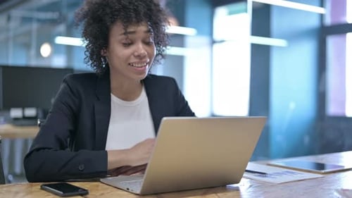 Cheerful African Businesswoman Doing Video Chat on Laptop in Office