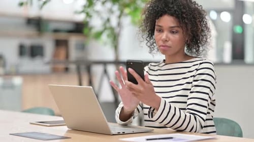 African Woman Using Smartphone and Laptop in Office