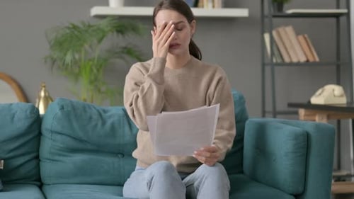 Worried Woman Reading Documents on Couch at Home