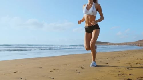 Beautiful Woman in Sports Shorts and T-shirt Running on the Beach with White Sand and Blue Ocean