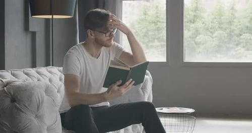 Young Man Reading a Book on the Sofa