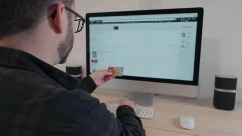 Young Adult Types at Computer While Holding Credit Card