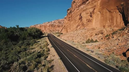 Drone Follows Silver Car Driving on Highway Between Big Steep Canyon Rocky Mountain, Bushy Desert
