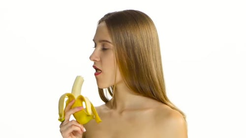 Young Woman Bites Into Banana on White Background