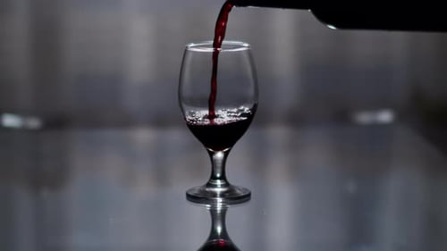 Silhouette of a glass with red wine pouring from a bottle, on a dark background