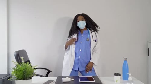 Black female doctor in medical mask dancing in clinic