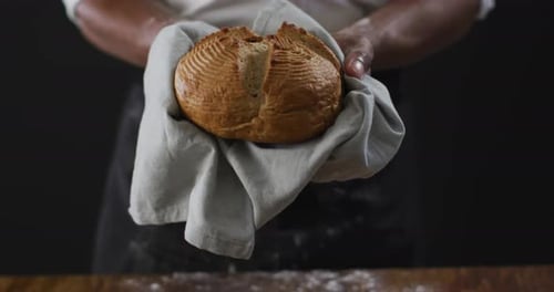 Video of cook holding loaf of bread on black background