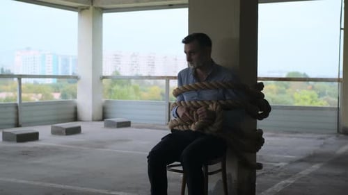 Un homme d'affaires en chemise est assis attaché avec une corde épaisse dans le parking