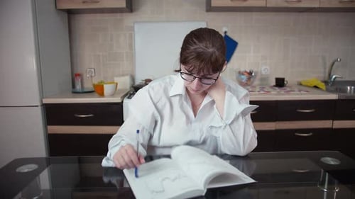 Woman Studying Book at Table in Kitchen