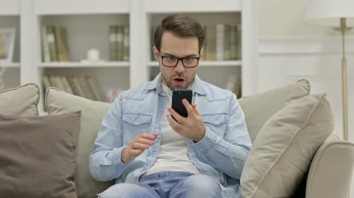 Man Celebrating Success While Using Smartphone on Sofa